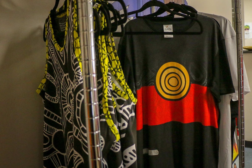 A t-shirt with the Aboriginal flag on it hangs on a rack.