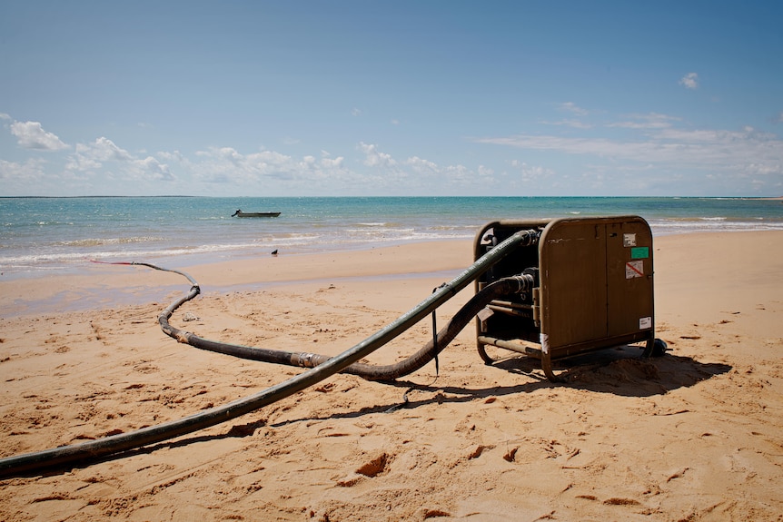 A small machine on a beach, with some piping running to it from the ocean, and another running away.