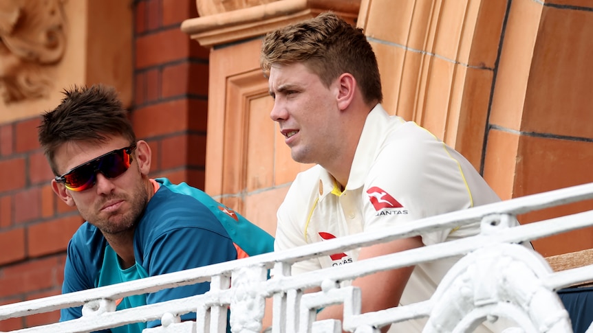 Australia Test players Mitch Marsh, in training gear and sunnies, and Cameron Green, in whites, talk on a balcony.