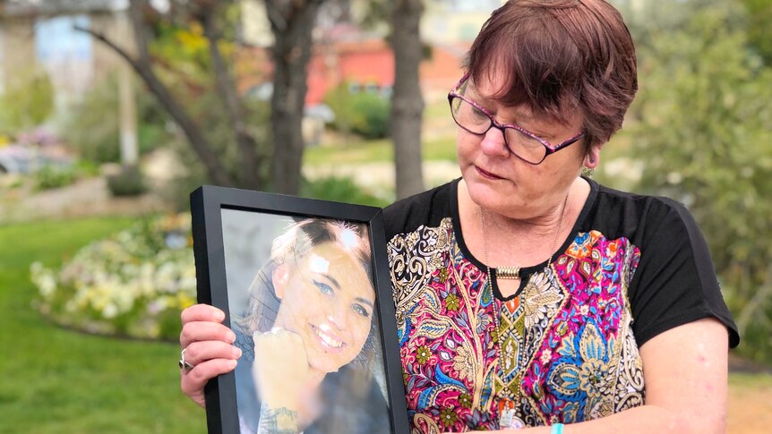 A woman holds a framed picture of her daughter.