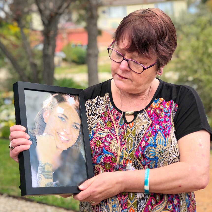 A woman holds a framed picture of her daughter.