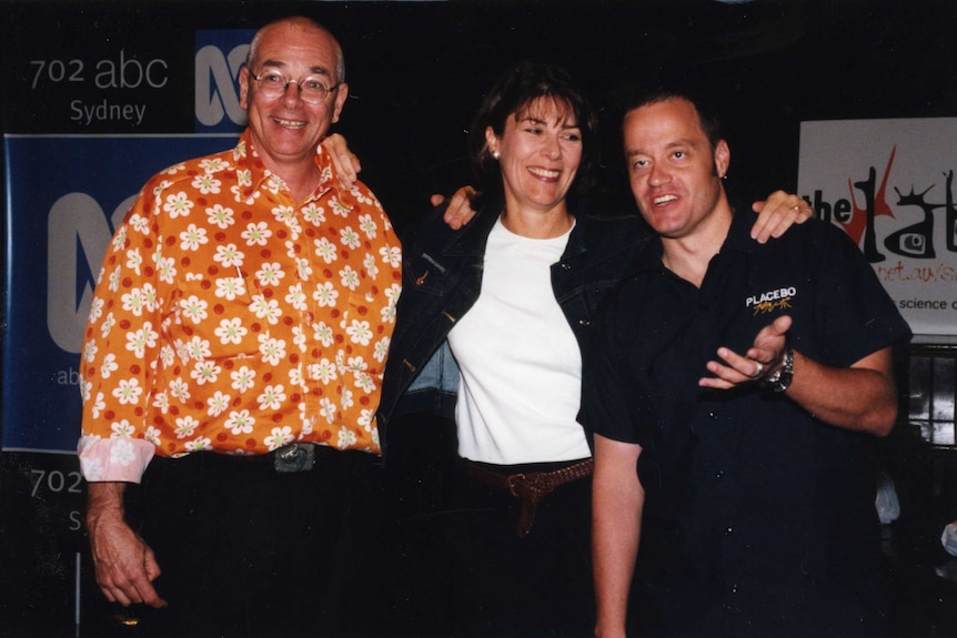 Two men and a woman stand with their arms around each other, ABC branding visible in the background.