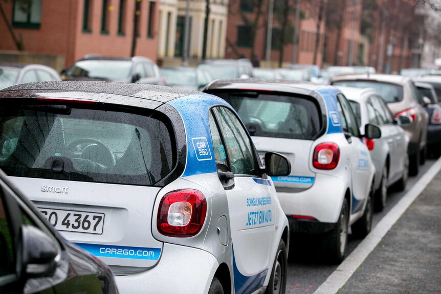 Two small cars with 'Car2Go' branding sit parked in a line of cars on the right hand side of a Berlin street.