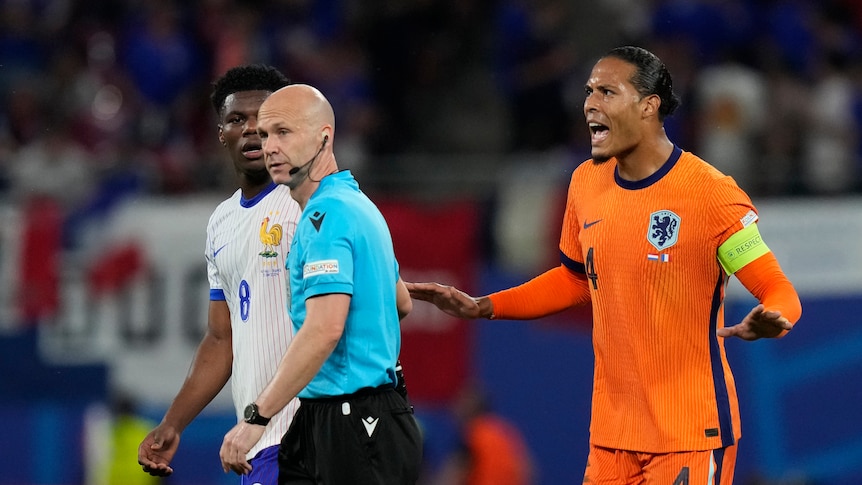 A referee walks away as an angry Dutch footballer stands gesticulating with his hands after a goal is ruled out.