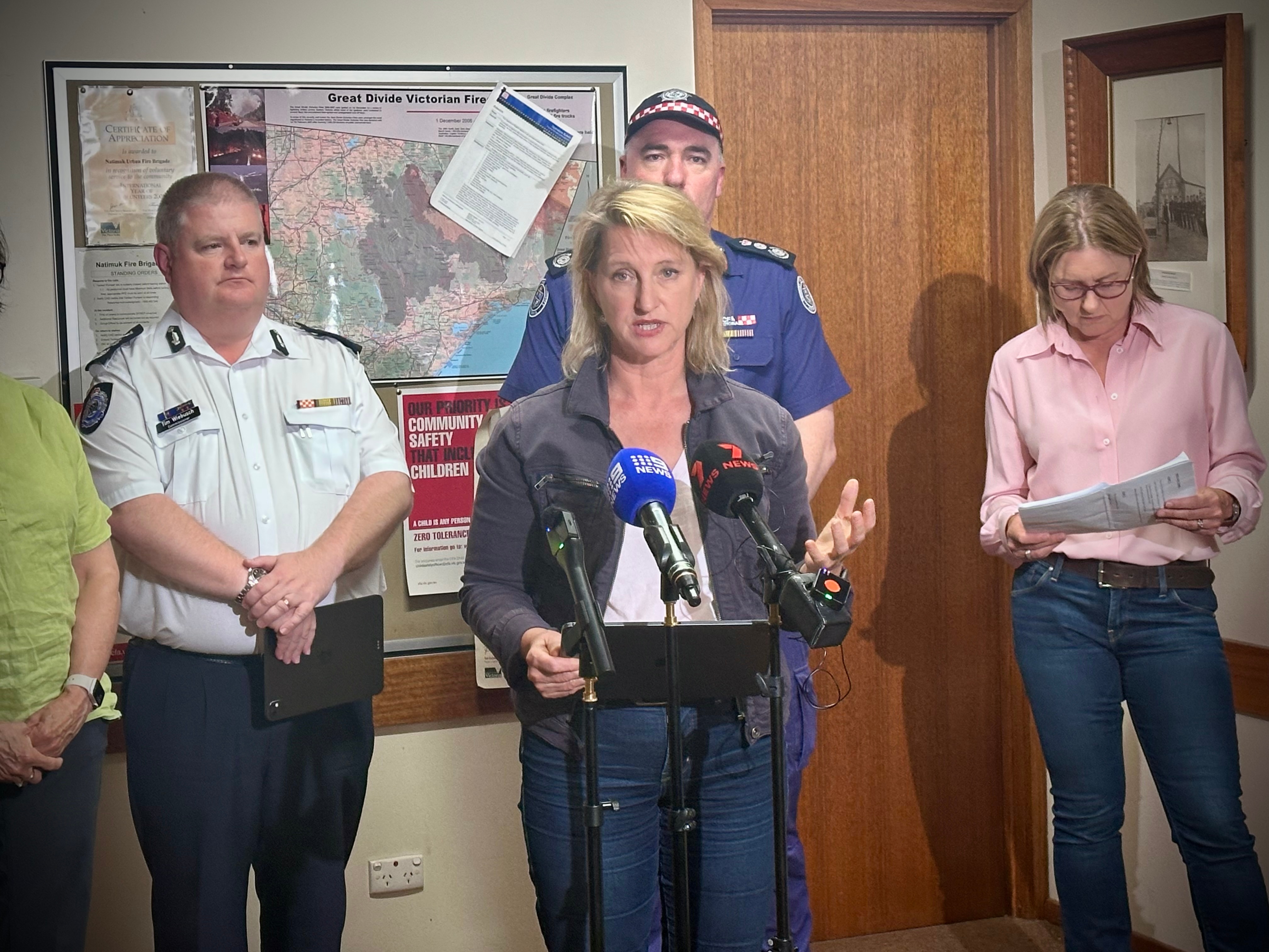 Emma Kealy, cabello rubio corto y chaqueta gris, habla frente a los micrófonos en un evento de prensa.