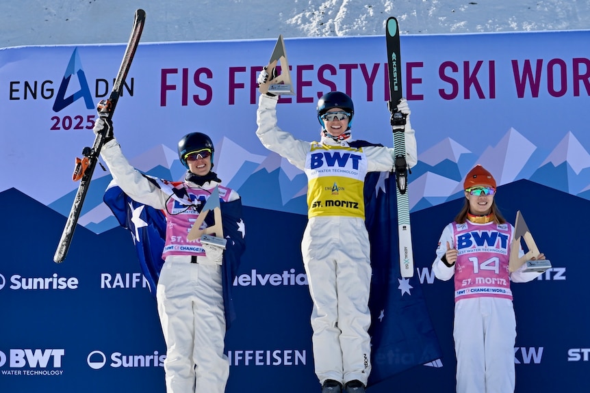 Three aerial skiers stand on a medal podium after a World Cup event in Switzerland.