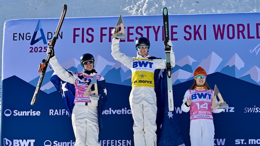 Three aerial skiers stand on a medal podium after a World Cup event in Switzerland.