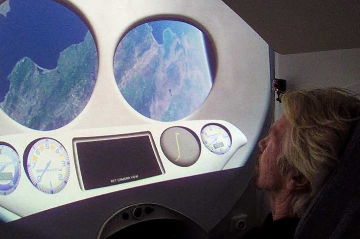 Richard Branson sits in front of a space capsule's windows.