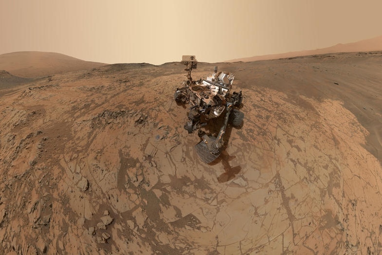 A photo of the Curiosity Mars rover robot on the red, dusty surface of Mars.