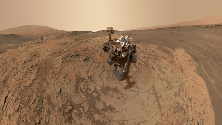 A photo of the Curiosity Mars rover robot on the red, dusty surface of Mars.