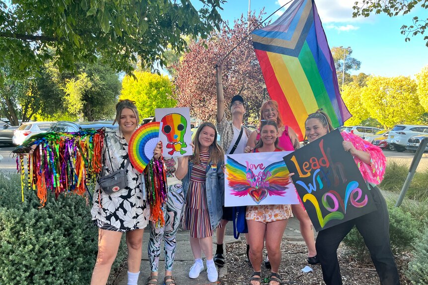 A group of young people carry rainbow flags and signs proclaiming support for the LGBTQIA+ community.
