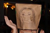 A person with a paper bag on their head with a self-portrait.