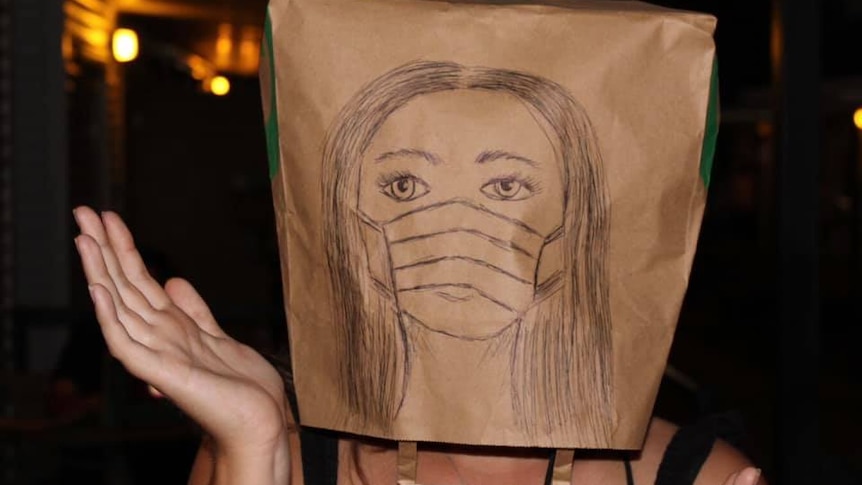 A person with a paper bag on their head with a self-portrait.