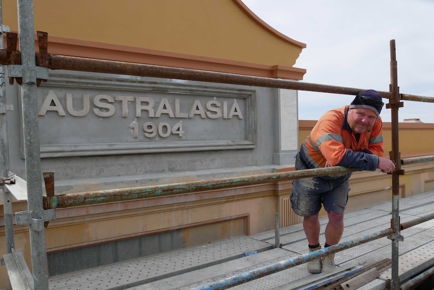 A man leans against structural beams with a concrete sign reading 'Australasia 1904' in the background.