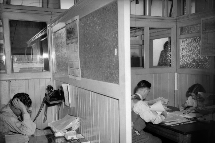 Black and white shot of people working at wooden desks in wood and glass cubicles