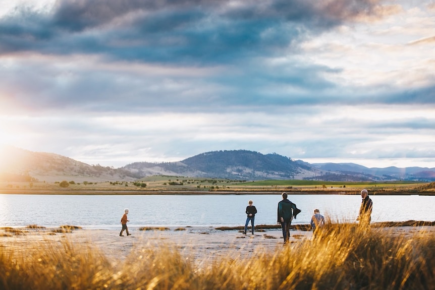 A handful of people stand at the banks of a river as the sun sets.