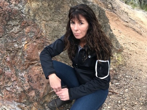 A woman crouching next to a small stone outcrop