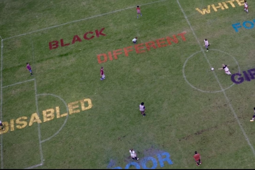Children playing on a field with words printed on it including disabled, black, different, white, girlie