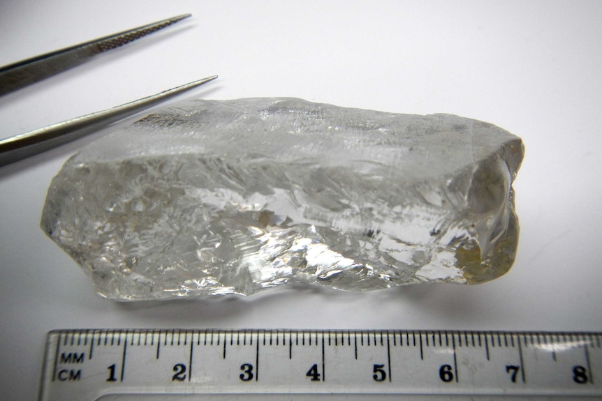 Large uncut diamond next to ruler and tweezers.