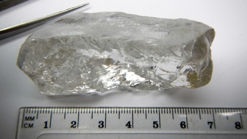 Large uncut diamond next to ruler and tweezers.