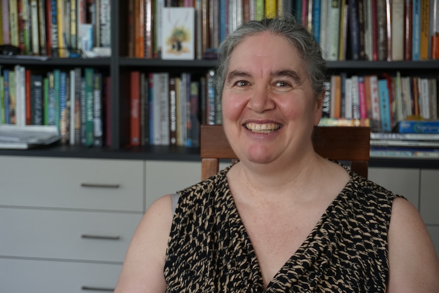 A smiling woman sits in front of a bookshelf.