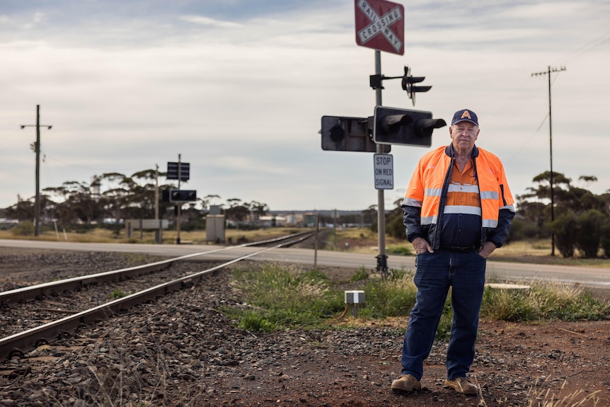 A male train driver wearing high-vis workwear stands near a level crossing.