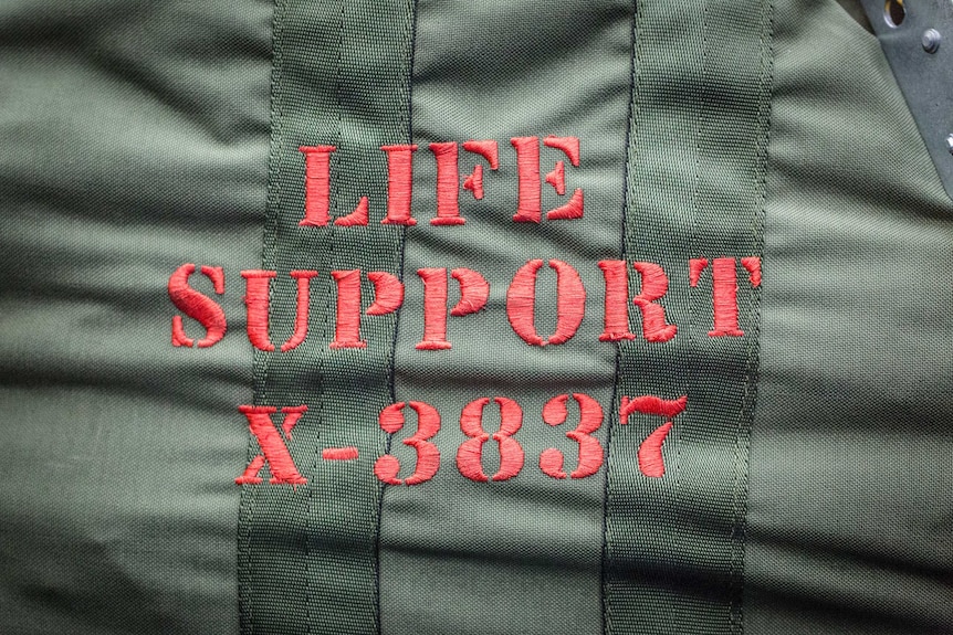 Close up of an army-green bag with the words "Life Support X-3837" embroidered on it.