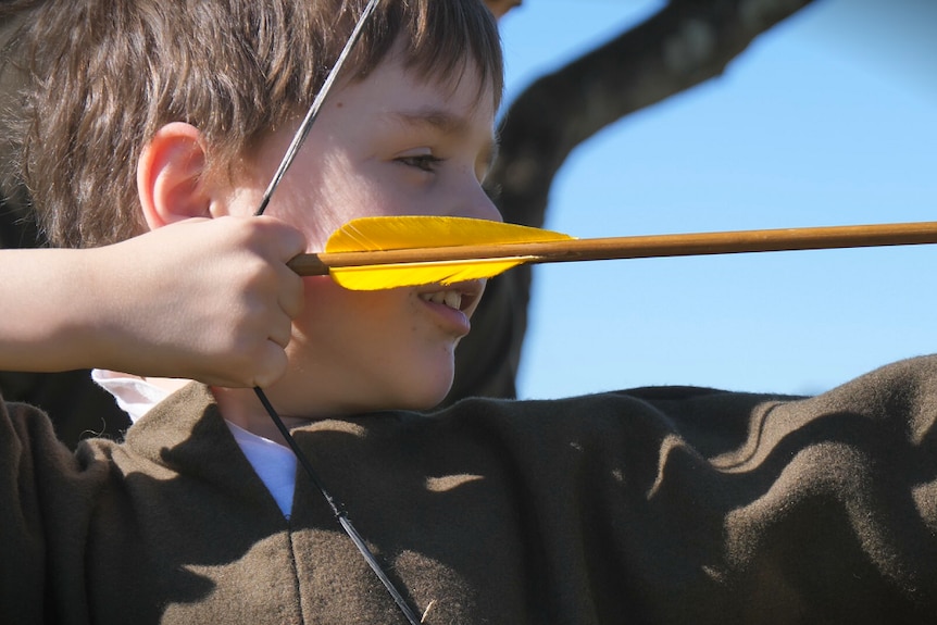 A young boy in a green shirt is pulling back a yellow arrow.