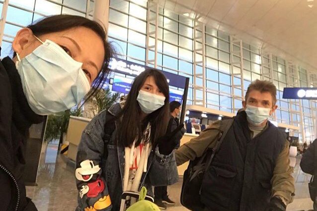 Three people stand in Wuhan's airport terminal wearing facemasks and taking a selfie.