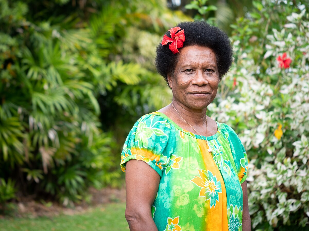 PNG woman with flower in hair standing in front of palm trees