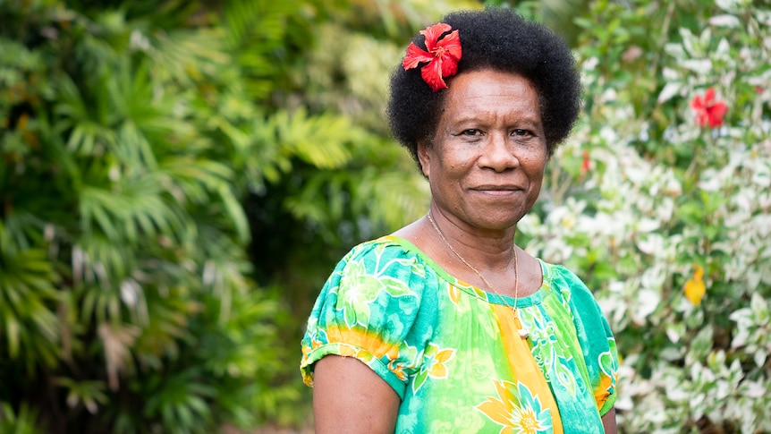 PNG woman with flower in hair standing in front of palm trees