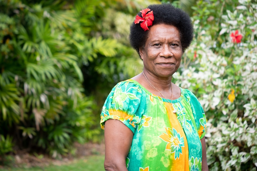 PNG woman with flower in hair standing in front of palm trees