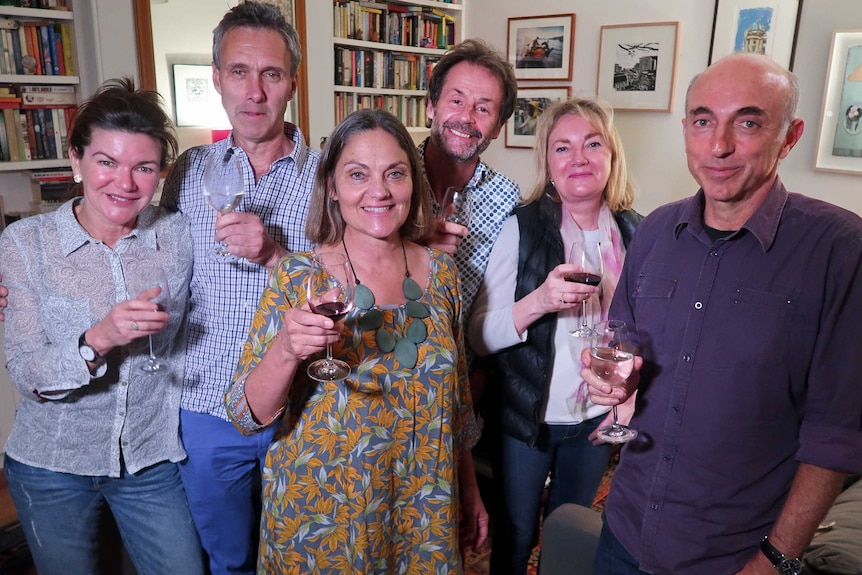 Six people smile for the camera holding wine glasses.