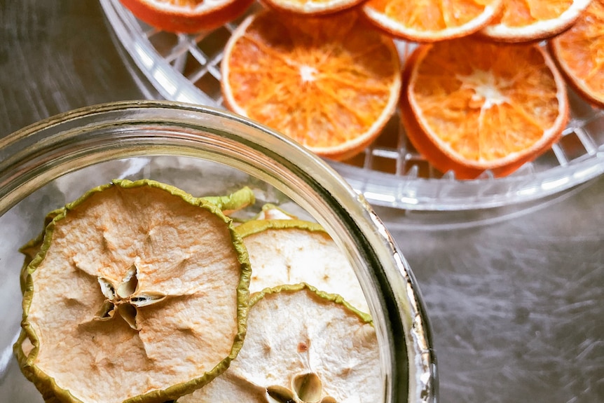 a bowl containing dried green apple slices and another bowl filled with dried orange slices