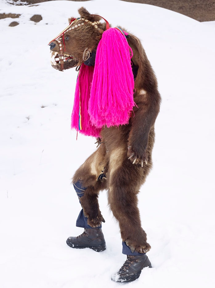 A man wearing bear skins for a European fertility ritual stands in the snow with a vivid pink scarf around his neck