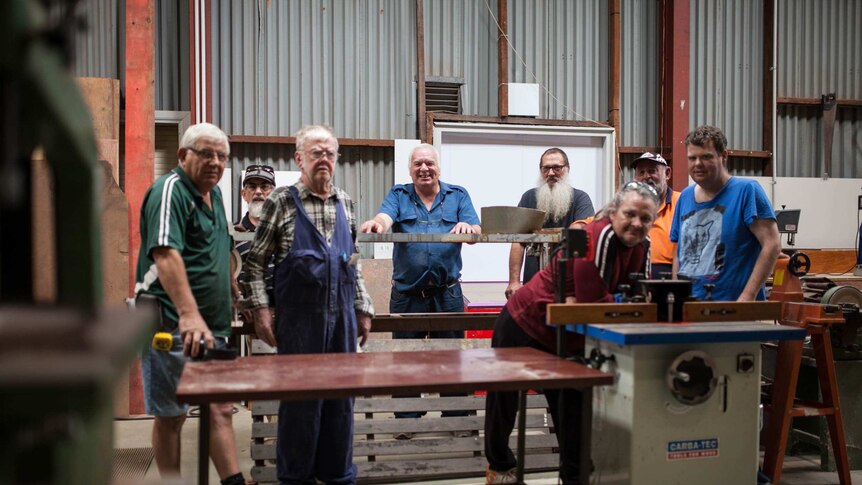 Men who attend the Kambalda men's shed in outback WA stand next to their equipment.