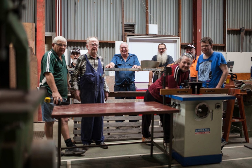 Men who attend the Kambalda men's shed in outback WA stand next to their equipment.