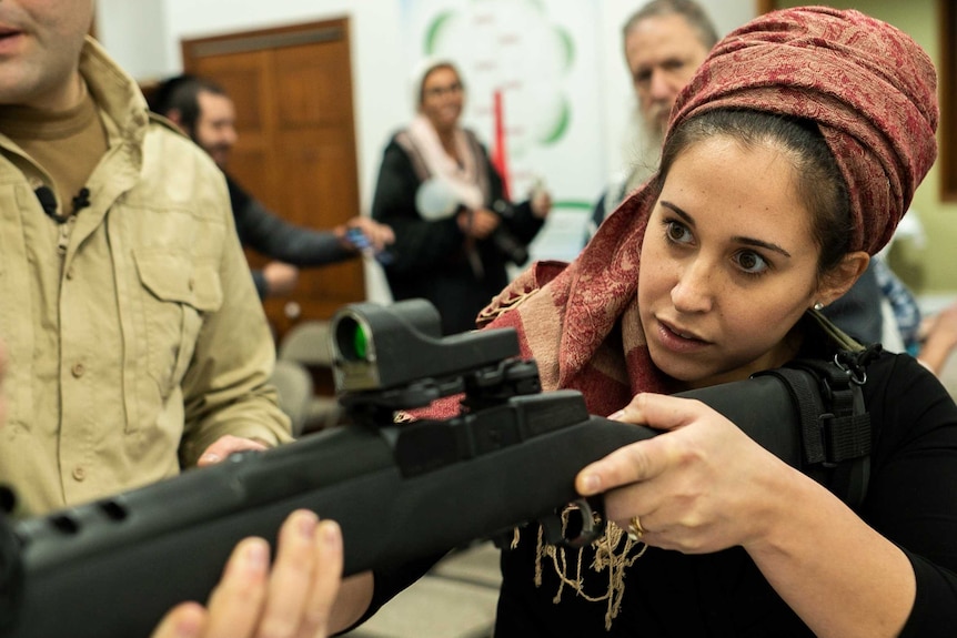 A woman holding a gun and looking toward a target while being instructed