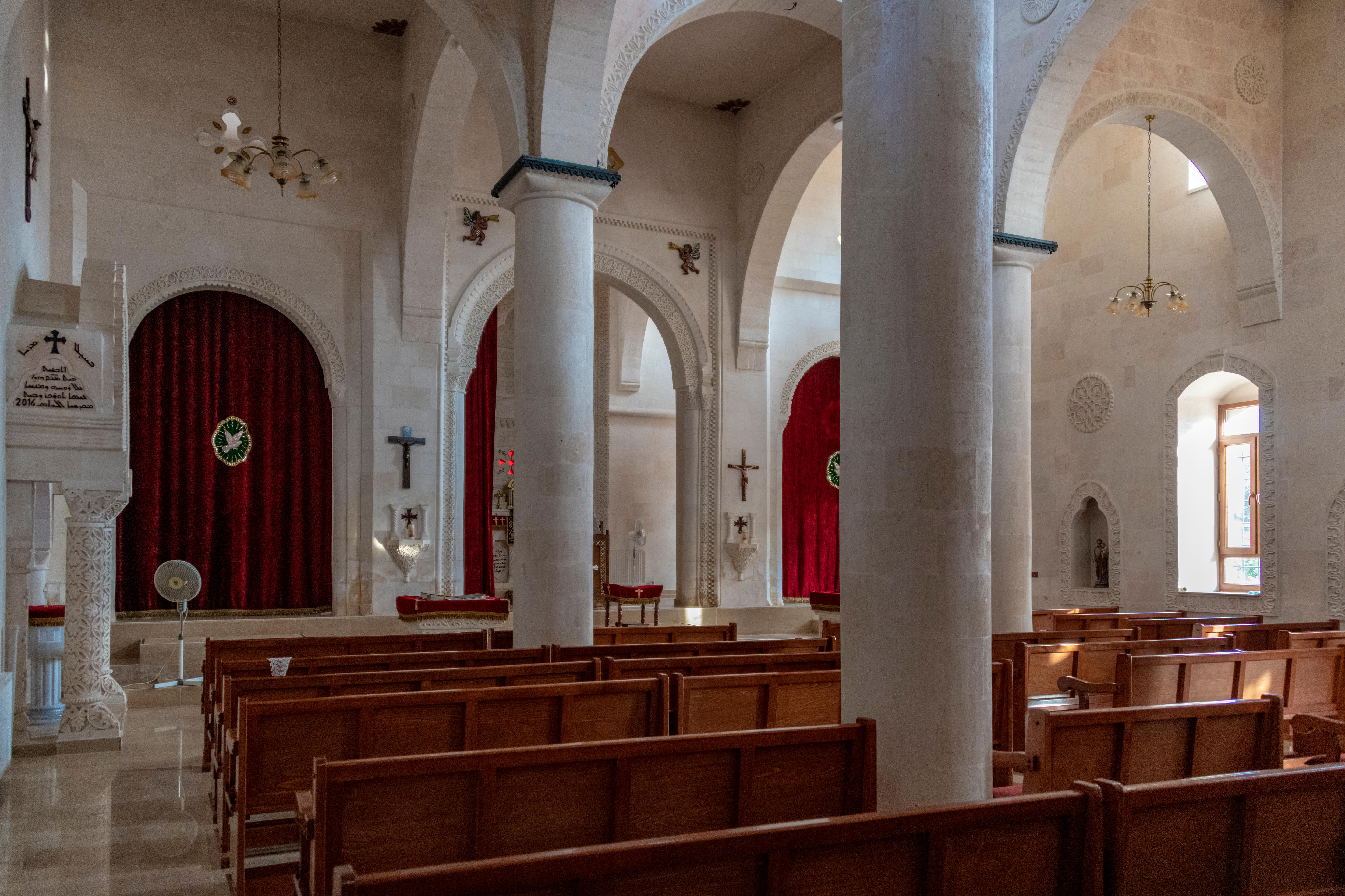 back view of empty wooden pew rows inside church, divided by large white pillars