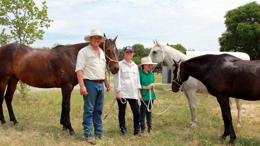 Family of three stand with their horses.