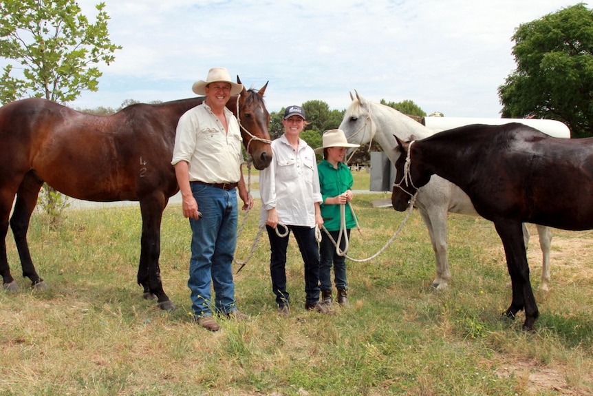 Family of three stand with their horses.