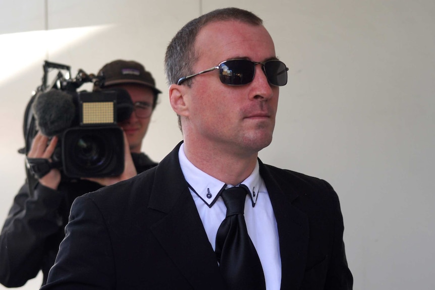 A mid shot of WA Police officer Andrew Barber outside a Perth court with a cameraman behind him.