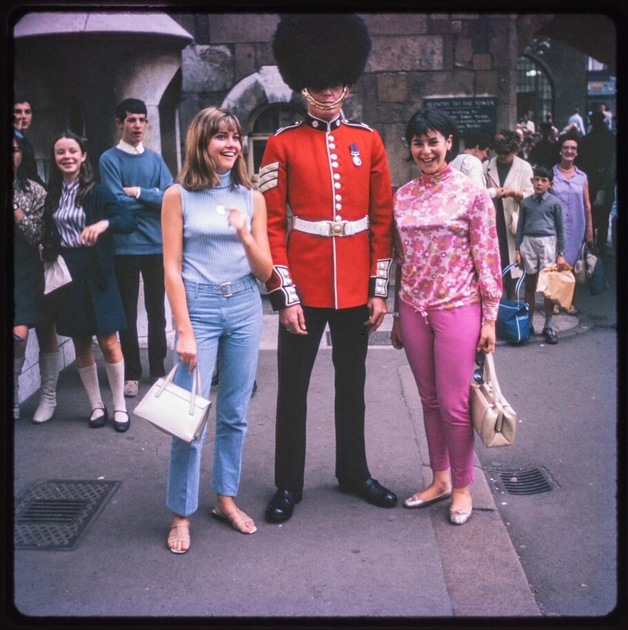 Two women in London during the 1960s, smiling near a Queen's guard.