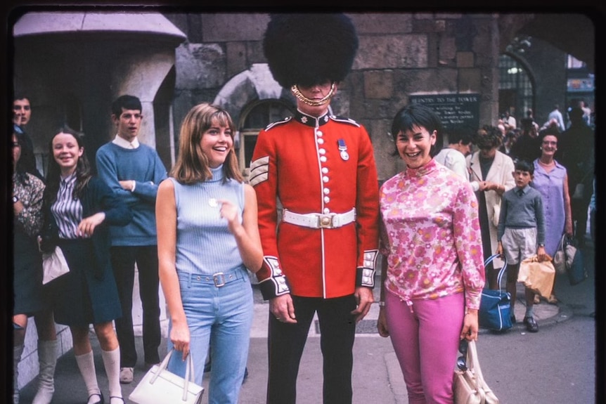 Two women in London during the 1960s, smiling near a Queen's guard.