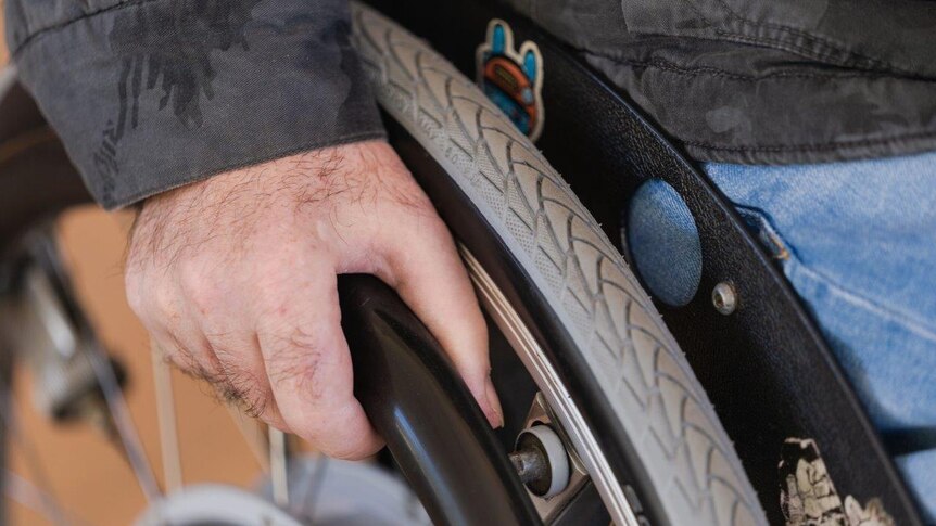 A close up photo of a man's hand on the wheel of a wheelchair.
