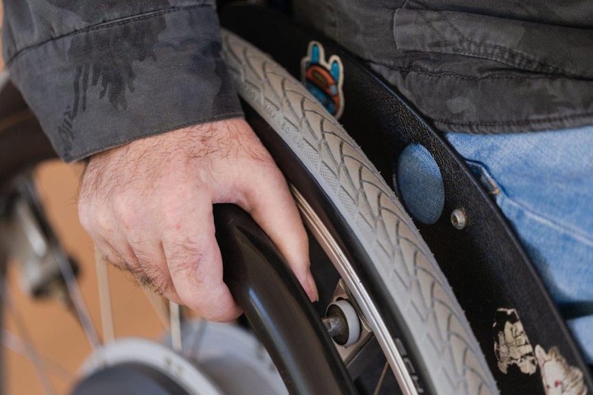 A close up photo of a man's hand on the wheel of a wheelchair.