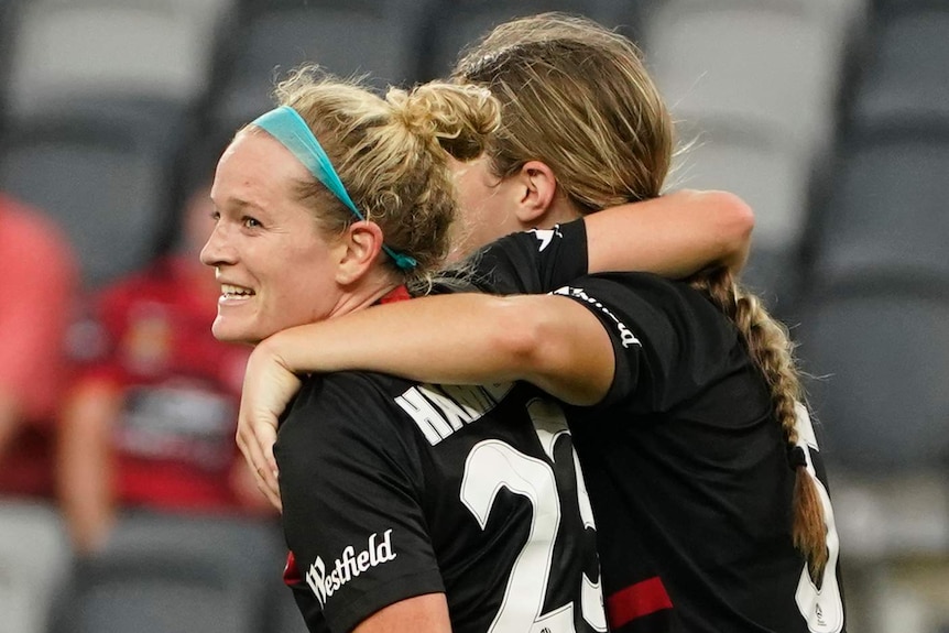 A Western Wanderers W-League player smiles as she celebrates a goal with a teammate against Perth Glory.