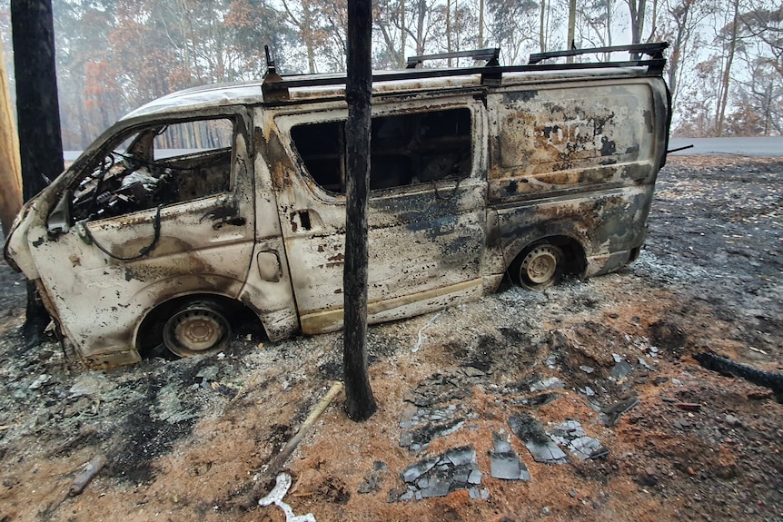 Burnt out white van surrounded by burnt trees and bare burnt earth