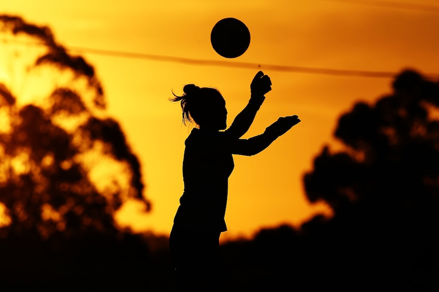 A soccer player catches a ball in a sunset