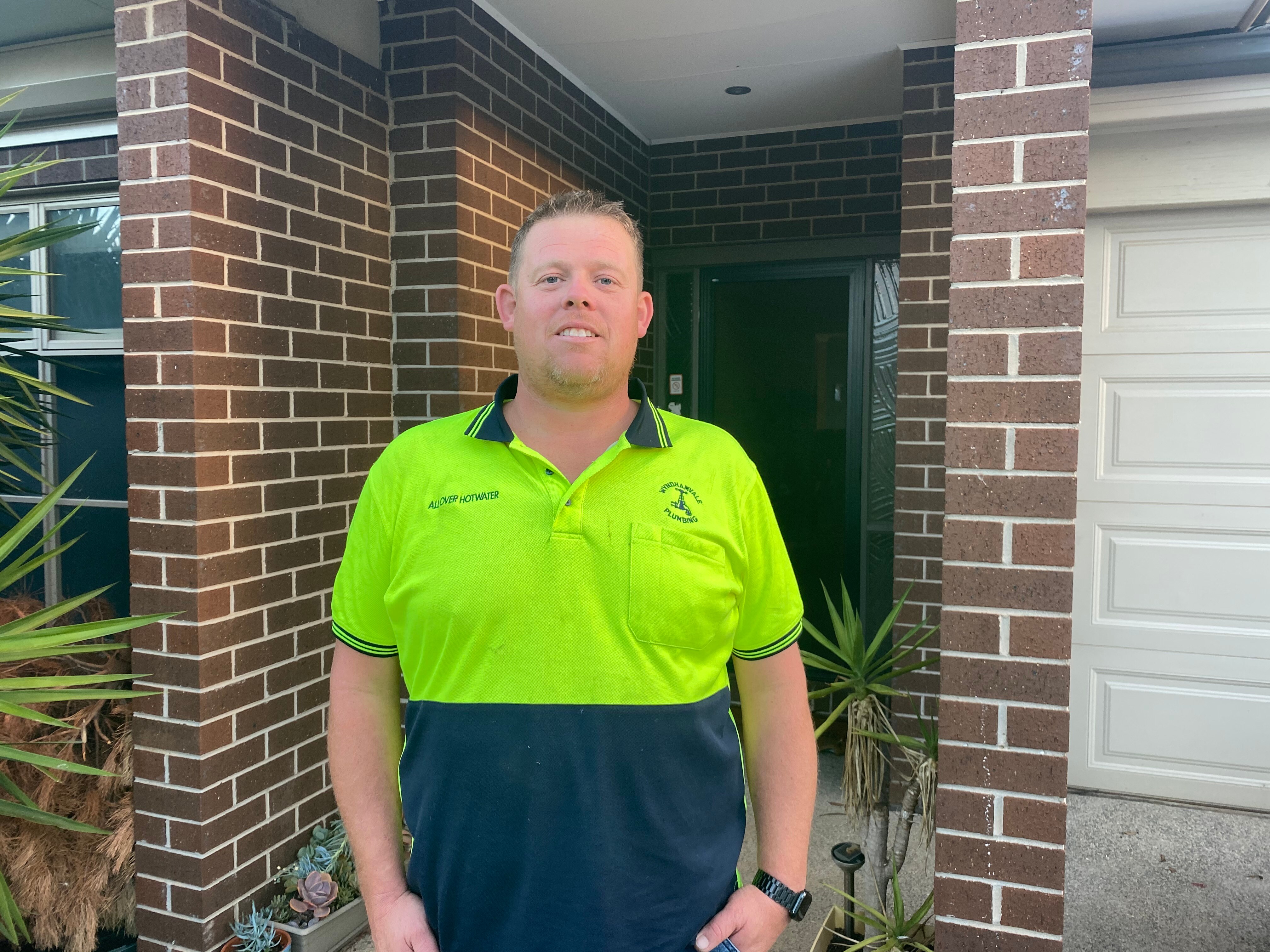 A man wearing a high-vis yellow shirt stands outside a house.